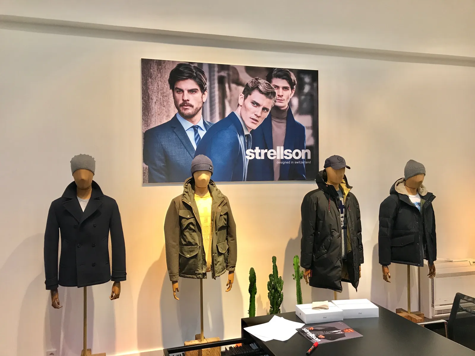 Cuatro maniquíes con abrigos y chaquetas de invierno ante una gran fotografía de campaña en una tienda de moda masculina