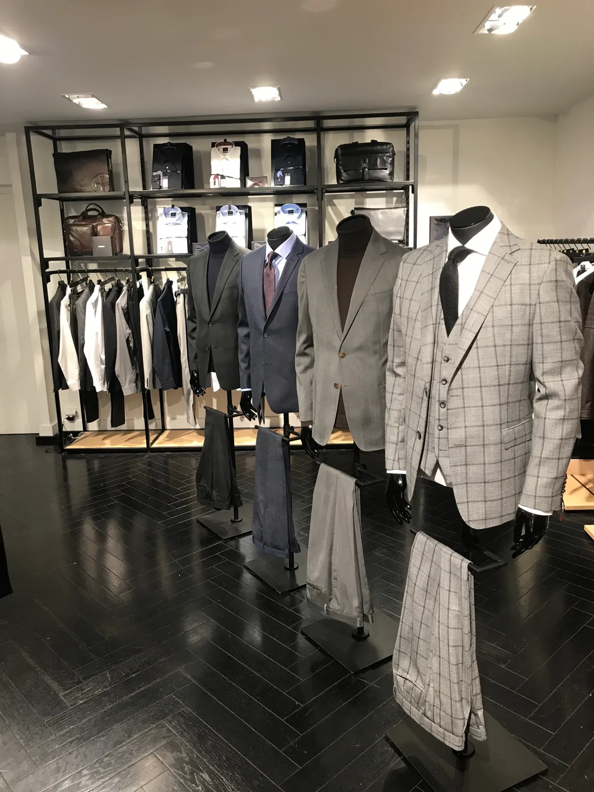 Sala de venta de una tienda de moda masculina con trajes en maniquíes, mesas de punto y estanterías iluminadas