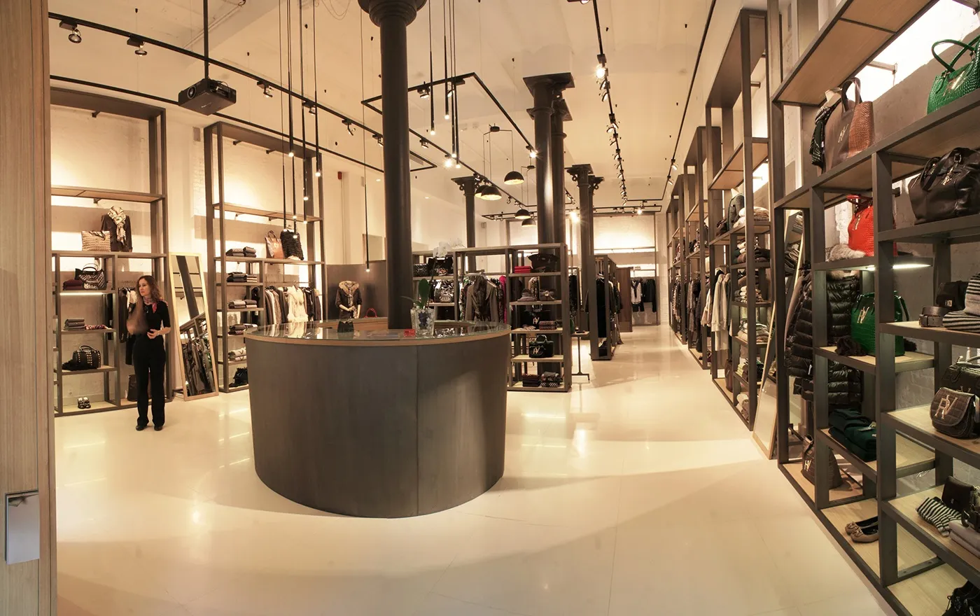 Interior de una tienda con mostrador circular en el centro y estanterías de bolsos y prendas a los lados